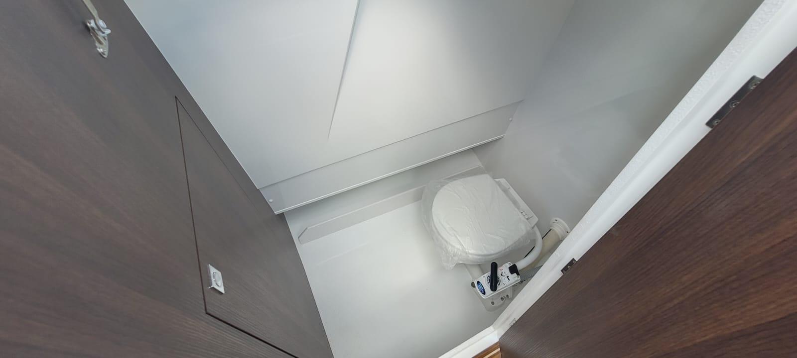 View of a modern bathroom featuring a white toilet wrapped in plastic, minimalist décor, and wooden door.